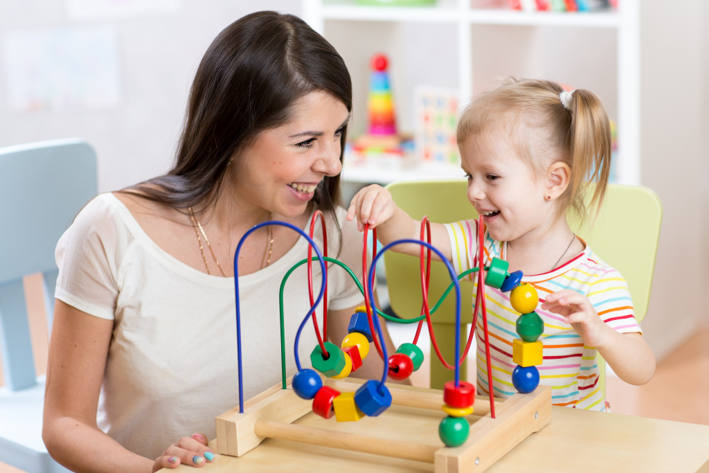 child and mother playing together with educational toy in nursery